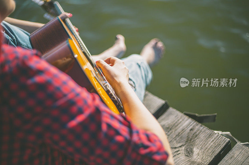 年轻女子坐在码头上弹吉他