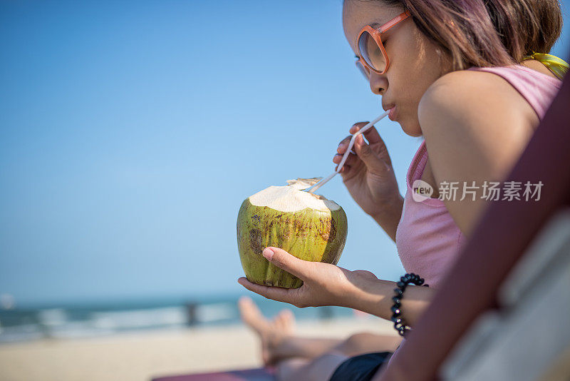 在海滩上享受日光浴的女人喝着新鲜的椰子