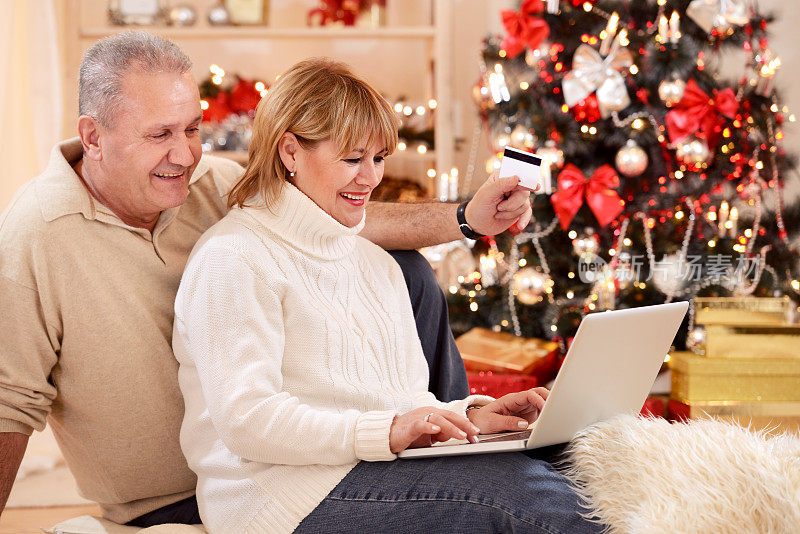 一对开朗成熟的夫妇正在用信用卡网购圣诞礼物