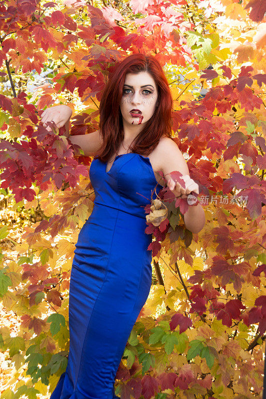 红发少年吸血鬼在蓝色的裙子，反对多彩的秋天灌木。