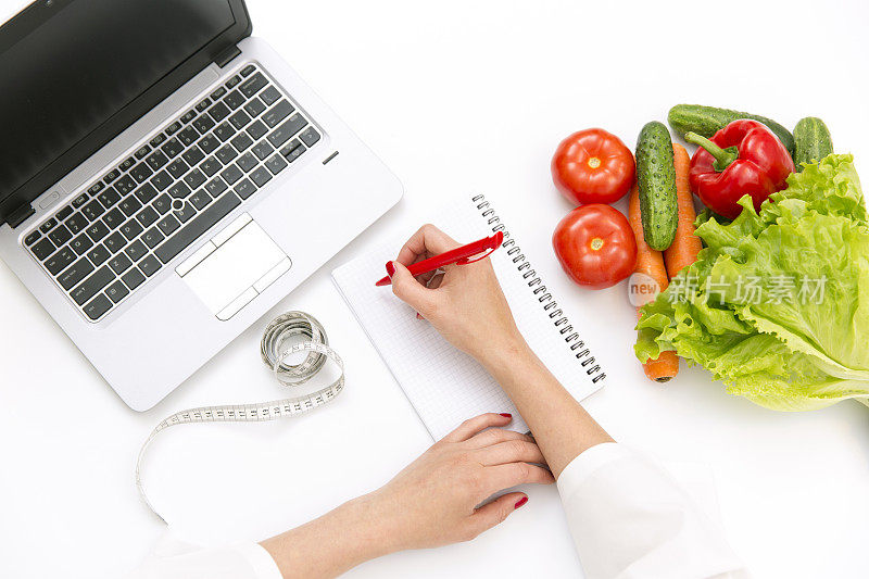 蔬菜饮食营养或药物概念。医生手写饮食计划，熟蔬菜成分，笔记本电脑和白底卷尺
