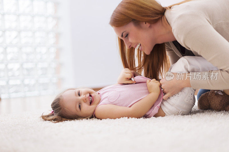 慈爱的母亲在家里的地毯上挠她的小女儿