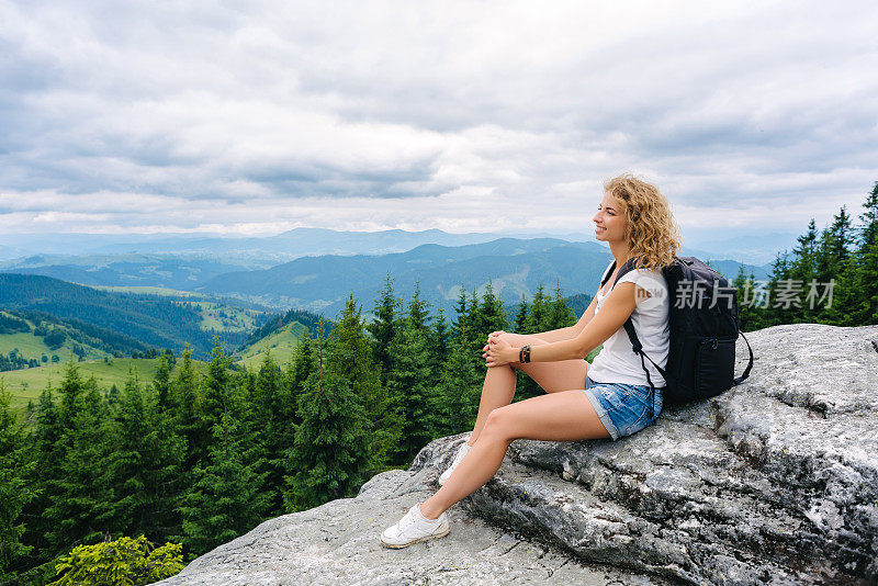 在多云的天气里，一个年轻的女孩站在山顶欣赏风景