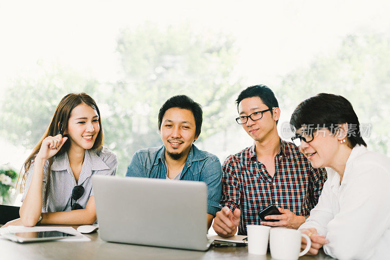 不同的亚洲商务同事或大学生在咖啡馆或现代办公室使用笔记本电脑在团队非正式会议，创业项目讨论或愉快的团队头脑风暴概念