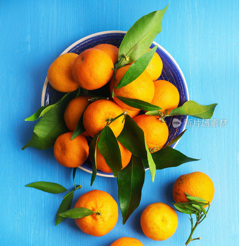 橘子(橘子，柑橘，小柑橘，柑橘类水果)，叶子放在蓝色盘子里，木质背景。有机素食。冬天当地的水果。健康排毒饮食观念。