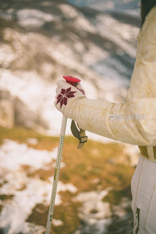 近景美丽的年轻女子在冬天的衣服站在一边，手拿木棍的背景雪山