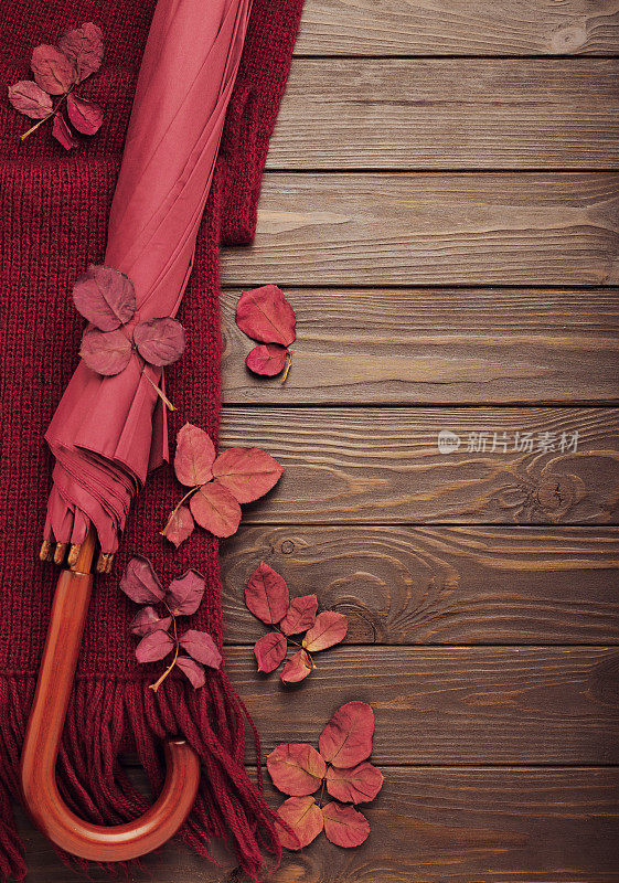 编织的紫红色围巾与秋天的叶子和伞在一个黑暗的木制背景。