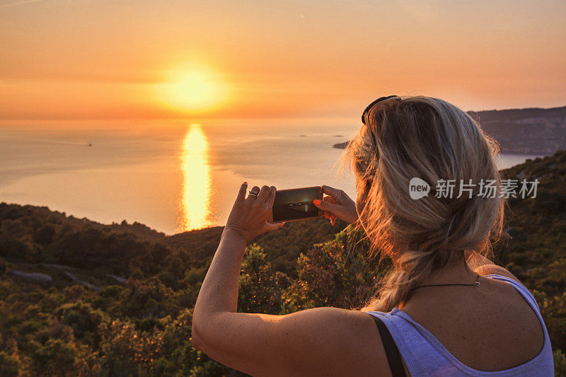 女人用智能手机在日落的地中海渔船拍照