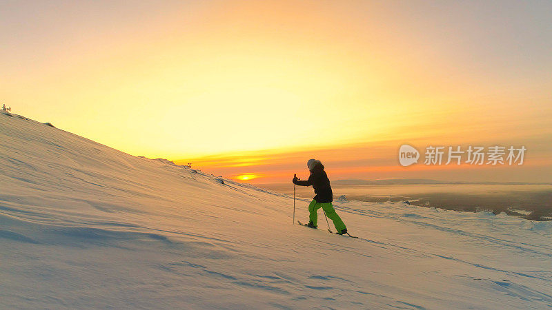 航拍:在金色的日出中，穿着雪鞋的运动女性走向雪山