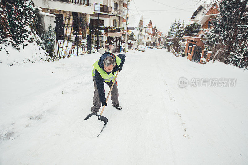 一个成熟的男人在清扫街上的积雪