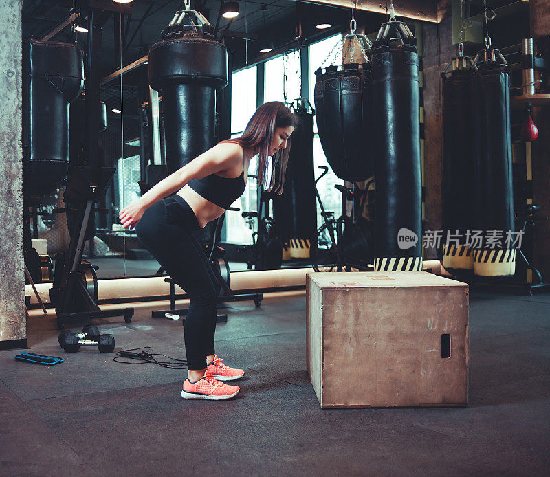 健身女跳上木箱在健身房训练，锻炼。穿着运动服的黑发女孩在健身房做跳跃运动