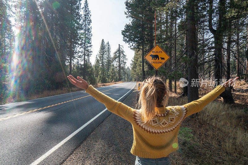 一名年轻女子张开双臂站在空旷的高速公路上，靠近熊的野生动物标志