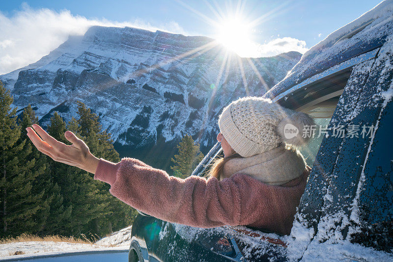 年轻女子在雪山公路上从车里伸出双臂