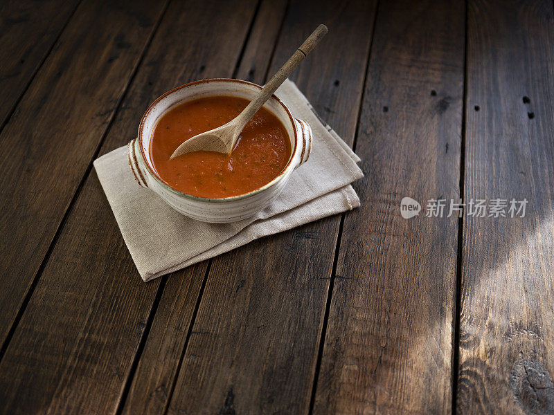 一碗西红柿罗勒汤，放在一个乡村碗里，靠在一张古老的深色木制桌子上。