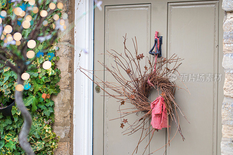 在科茨沃尔德郡格洛斯特郡的塞伦塞斯特，装饰节日的手工树枝花环挂在一扇古老的小屋木板门上。