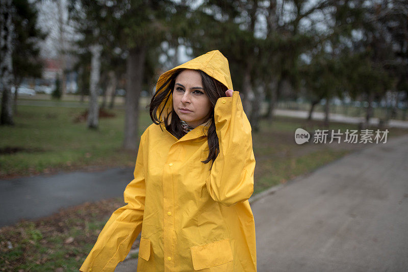 穿着黄色雨衣的年轻女子在公园里度过雨天