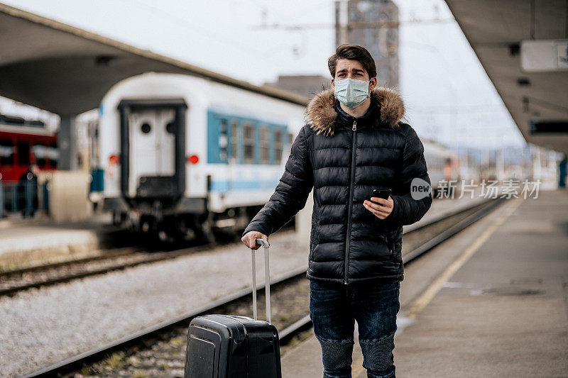 一名年轻男子戴着防护口罩在火车站等车