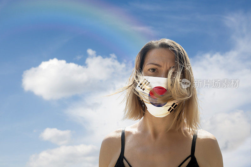 一名妇女戴着韩国国旗防护面具，在彩虹云景中躲避新冠肺炎