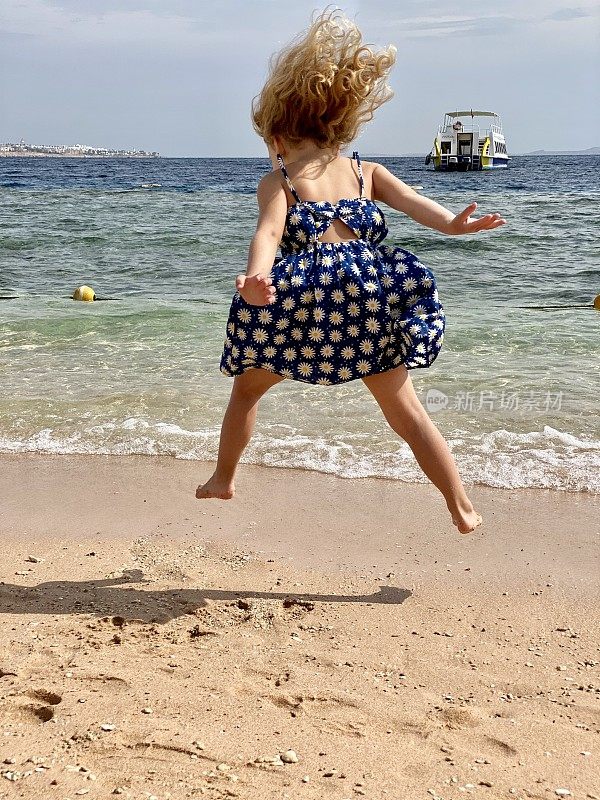 小女孩在海边的沙滩上蹦蹦跳跳。