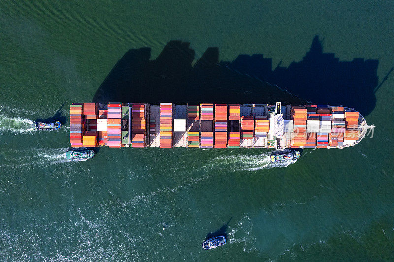 集装箱船满载驶近港口由拖船占据港口国际集装箱船在海上港口装卸货物，货运，航运，船舶。物流，进出口，运输。全球运输b