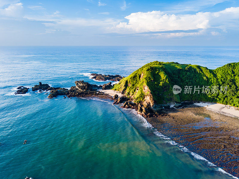 鸟瞰图一个郁郁葱葱的绿色山坡的海洋，清澈的蓝色海水，岩石海岸线，多云的天空，龙目岛。