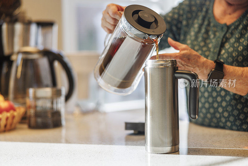 热水杯里的茶可以保持几个小时的热度:在厨房里，老妇人用手把茶倒进绝缘的饮料容器里