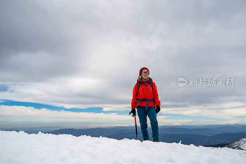 一位女登山者站在高海拔的山顶上，手持冰镐看着镜头。