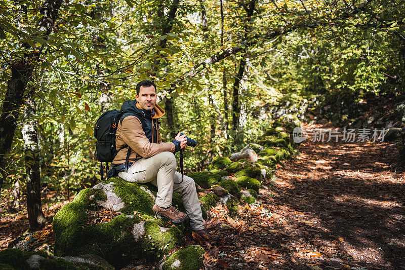 年轻而美丽的摄影师在散步和拍摄环境奇观后，在森林的一块石头上休息的侧面肖像