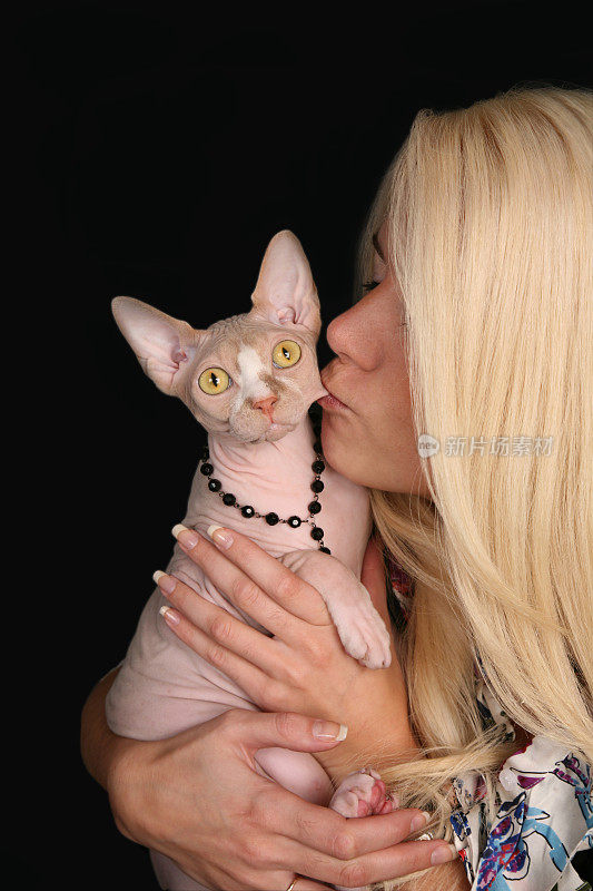 金发的年轻女士抱着她的斯芬克斯猫亲吻脸颊