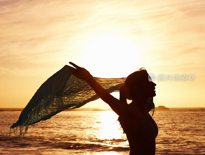 日落时分，在海边，一个女人拿着纱笼的剪影