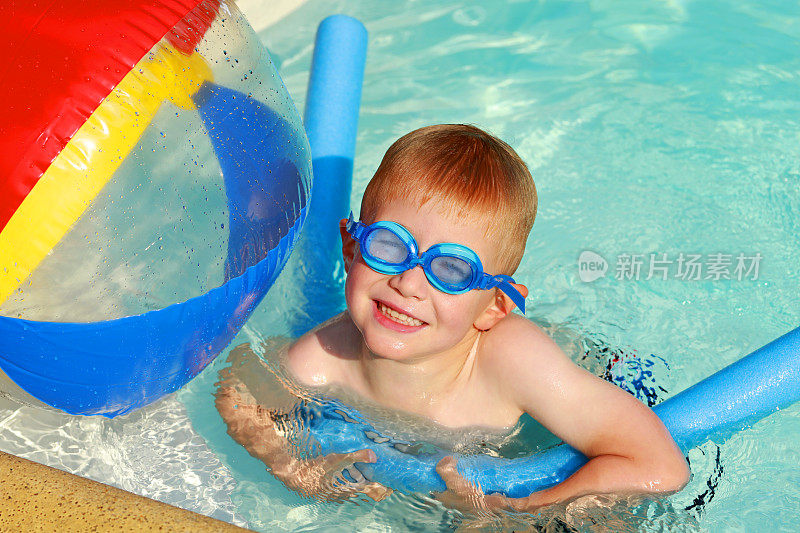 孩子与沙滩球和面条浮在游泳池