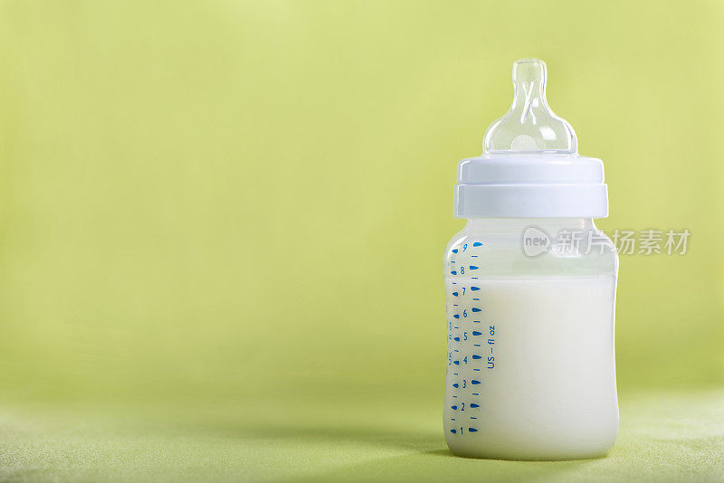 绿色床单上放着牛奶的婴儿奶瓶