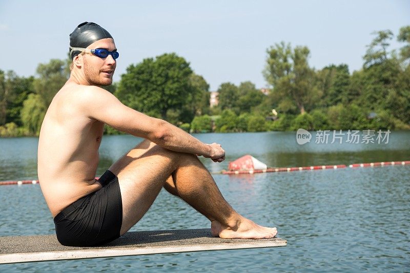 一个人坐在湖边阳光下的跳水板上