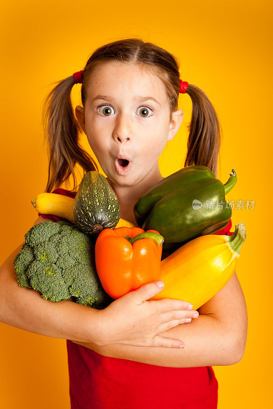 惊讶的小女孩拿着蔬菜，青椒，花椰菜，南瓜，西葫芦