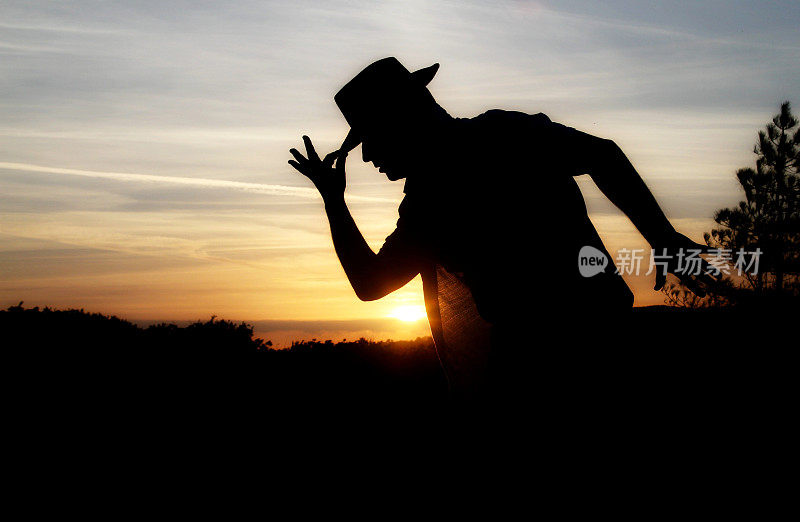 日落时戴着帽子跳舞的男人的剪影
