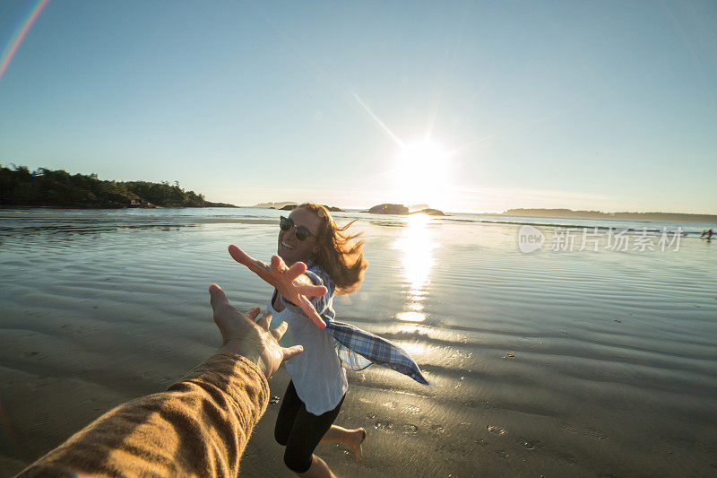 一个年轻女子在海滩上跑向一个男人的手