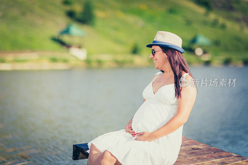 一个怀孕的女孩坐在河边的木桥上