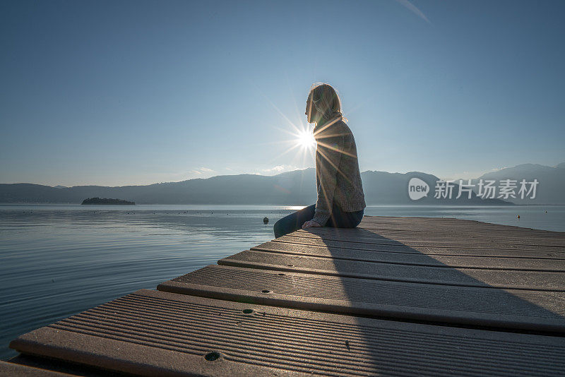 年轻女子在湖边码头休息，看日落