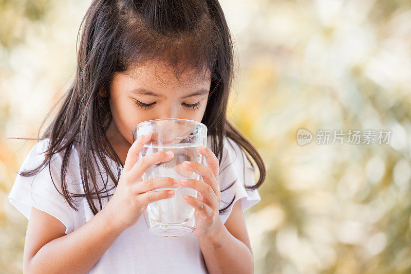 可爱的亚洲小女孩饮用新鲜的水从玻璃在复古色调