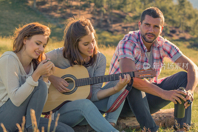 一个年轻女子和朋友在日落室外弹吉他唱歌