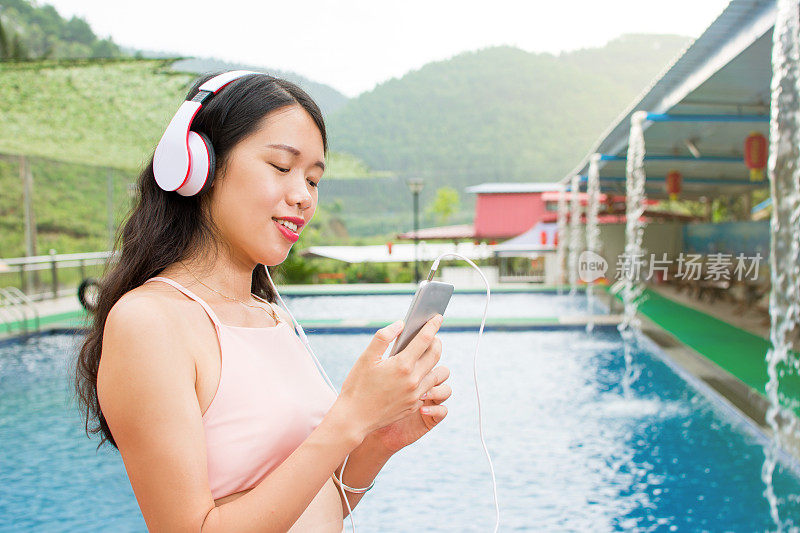 女孩拿着手机在游泳池边听音乐