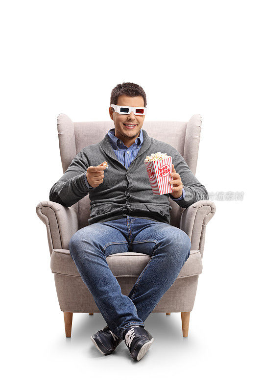 一名年轻人戴着3D眼镜坐在扶手椅上吃着爆米花