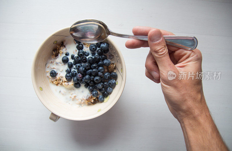 用勺子拿早餐麦片，里面有蓝莓和牛奶