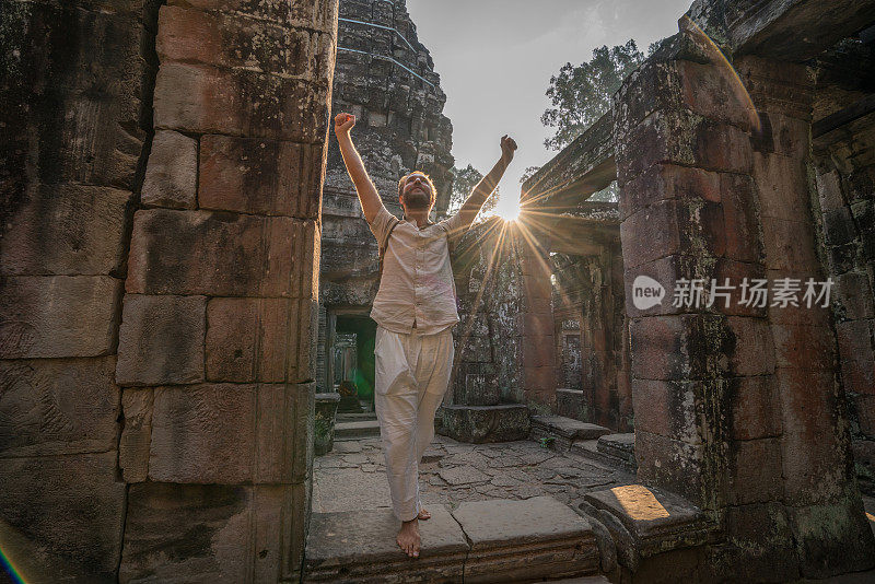 一名年轻男子在柬埔寨参观吴哥窟的庙宇，他张开双臂站着。人们旅游发现亚洲的概念。日落时分，只有一个人，在东南亚暹粒冒险和探险。