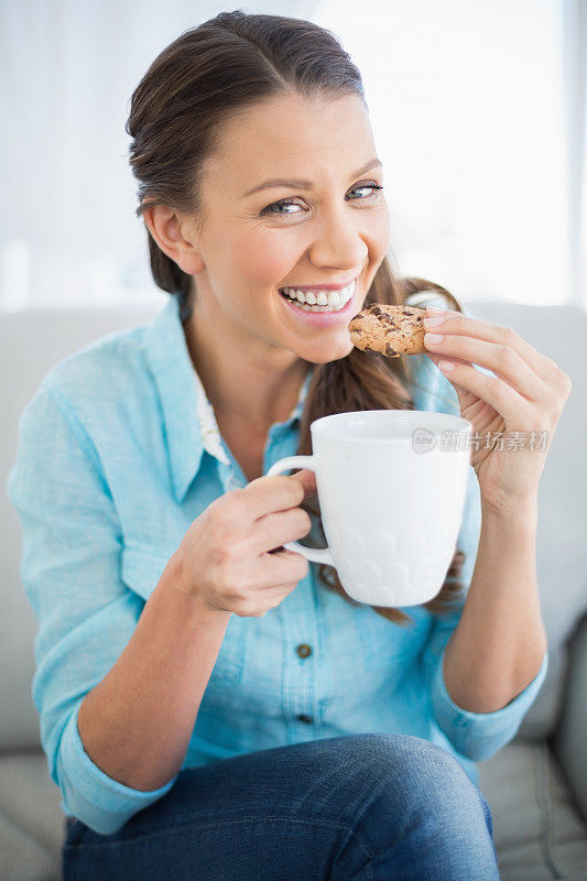 微笑的女人拿着一杯咖啡吃饼干