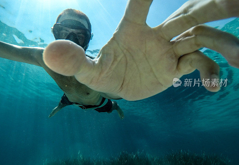 在清澈温暖的海水中，潜水员把手伸向相机