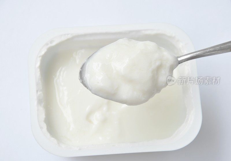 用勺子从白色背景的杯子里舀酸奶