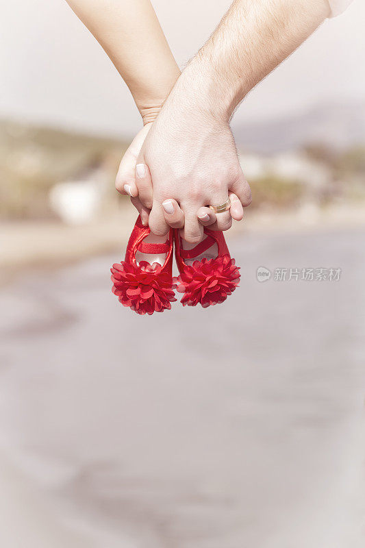 日落时分，一对怀孕的夫妇手牵着手，穿着红色婴儿鞋
