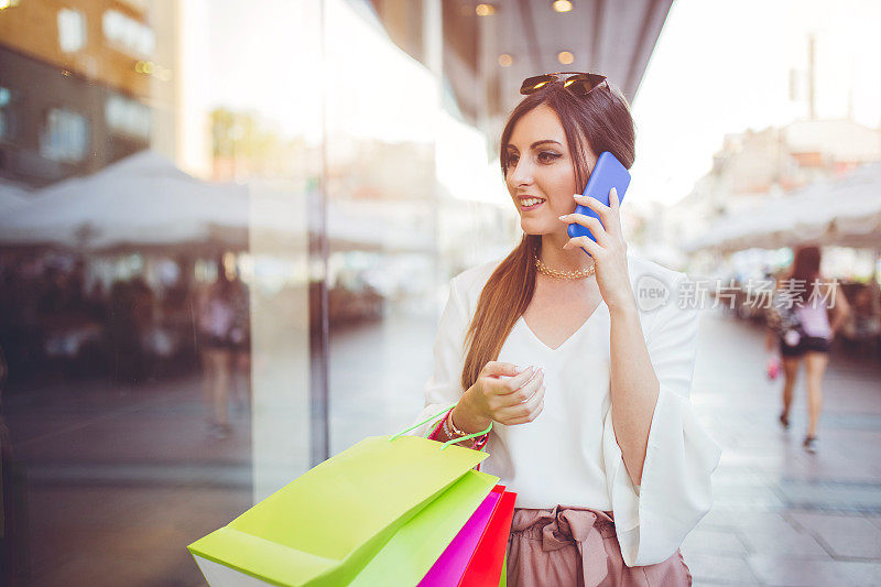一个女人走在商店橱窗附近，正在打手机。