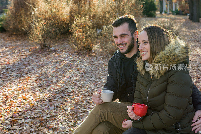 一对年轻夫妇坐在公园长椅上喝咖啡